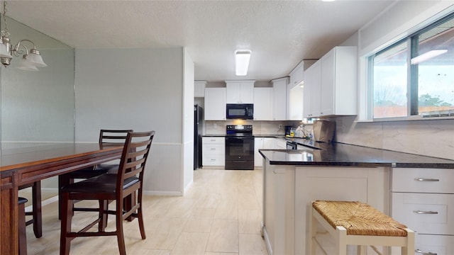 kitchen with pendant lighting, white cabinets, black appliances, sink, and decorative backsplash