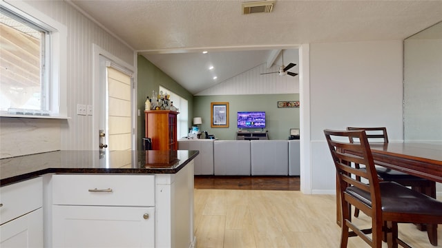 kitchen with kitchen peninsula, ceiling fan, light hardwood / wood-style flooring, vaulted ceiling with beams, and white cabinetry