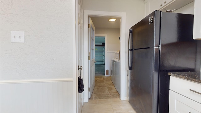 kitchen with washing machine and dryer, black refrigerator, white cabinets, and dark stone counters