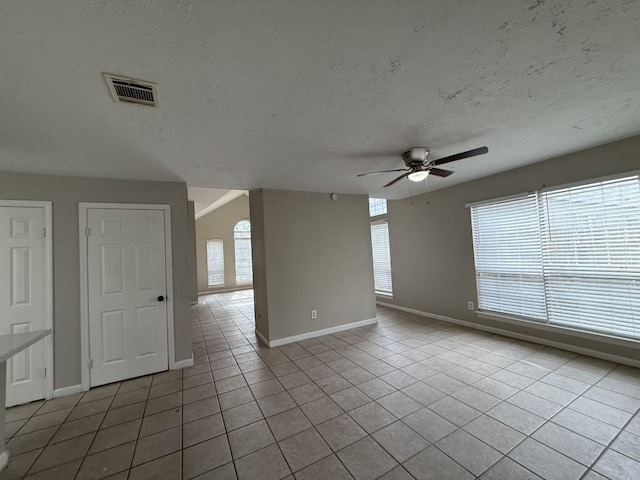 tiled empty room featuring ceiling fan, a wealth of natural light, and a textured ceiling