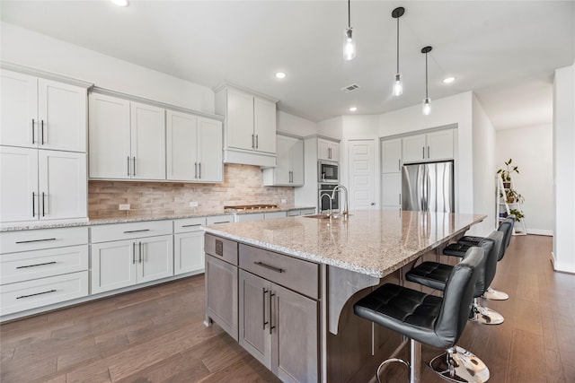 kitchen with a kitchen bar, light stone counters, stainless steel appliances, a kitchen island with sink, and sink