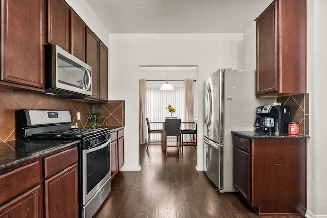 kitchen featuring dark wood-type flooring, hanging light fixtures, stainless steel appliances, backsplash, and dark stone counters