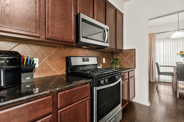 kitchen with pendant lighting, backsplash, dark stone countertops, appliances with stainless steel finishes, and dark hardwood / wood-style flooring