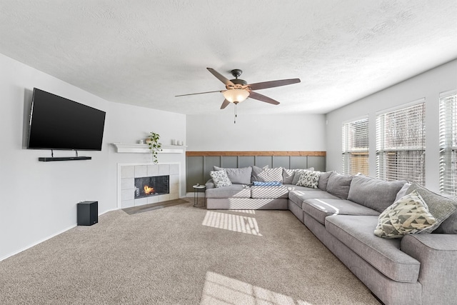 living room with a tile fireplace, ceiling fan, carpet floors, and a textured ceiling