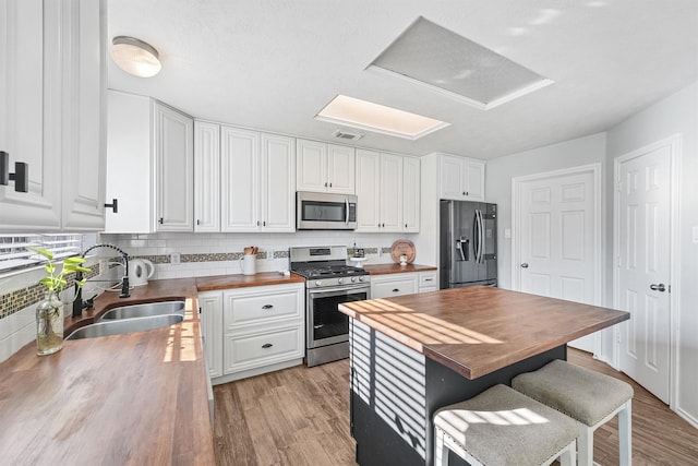 kitchen with wooden counters, appliances with stainless steel finishes, light wood-type flooring, sink, and white cabinetry