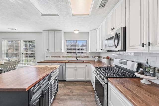 kitchen with decorative backsplash, appliances with stainless steel finishes, sink, white cabinetry, and butcher block counters