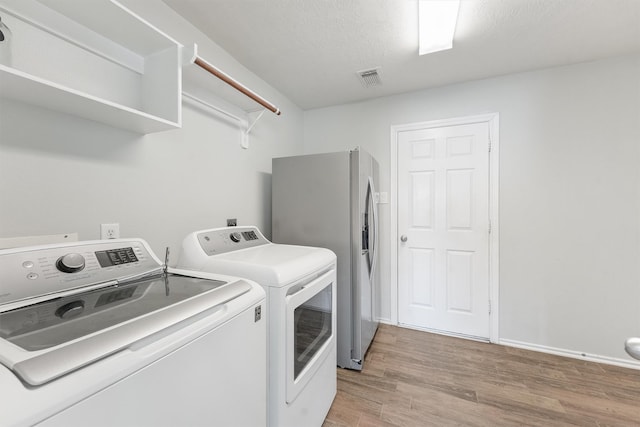 clothes washing area featuring washer and dryer, light hardwood / wood-style floors, and a textured ceiling