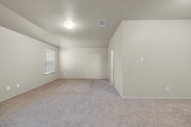 empty room featuring vaulted ceiling, light colored carpet, and a textured ceiling