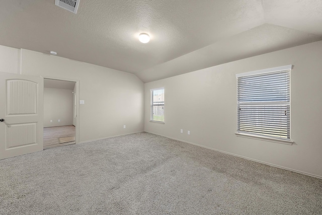 carpeted spare room with a textured ceiling and vaulted ceiling