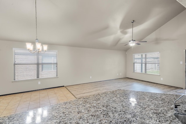 unfurnished living room with ceiling fan with notable chandelier, a healthy amount of sunlight, lofted ceiling, and light tile patterned floors