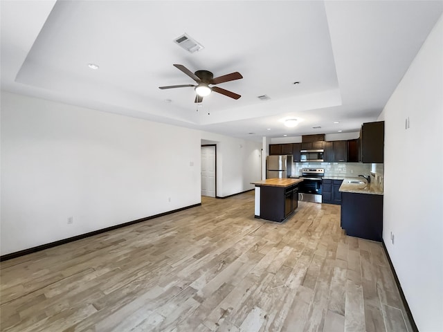 kitchen with wood counters, appliances with stainless steel finishes, a tray ceiling, and a kitchen island