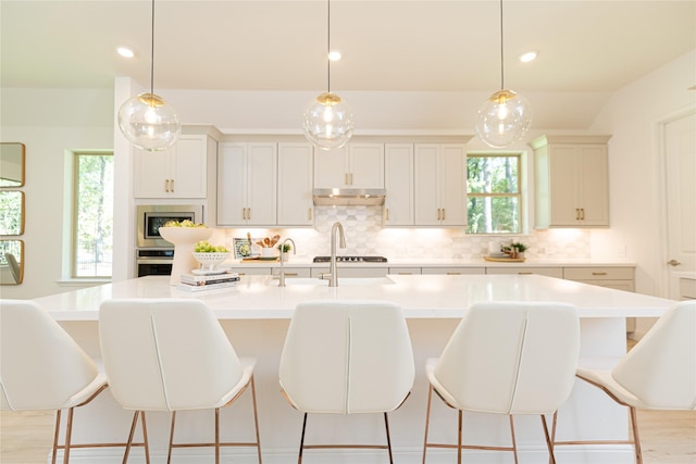 kitchen featuring decorative backsplash, an island with sink, stainless steel appliances, and decorative light fixtures