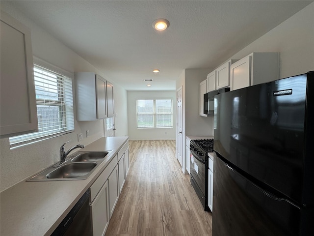 kitchen with sink, black appliances, light hardwood / wood-style floors, white cabinetry, and plenty of natural light