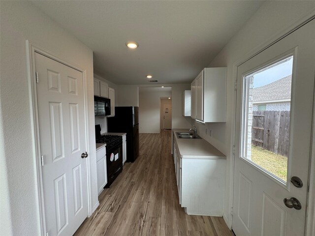 kitchen with black appliances, sink, light wood-type flooring, plenty of natural light, and white cabinetry