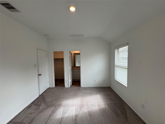 unfurnished bedroom featuring connected bathroom, a spacious closet, dark colored carpet, vaulted ceiling, and a closet