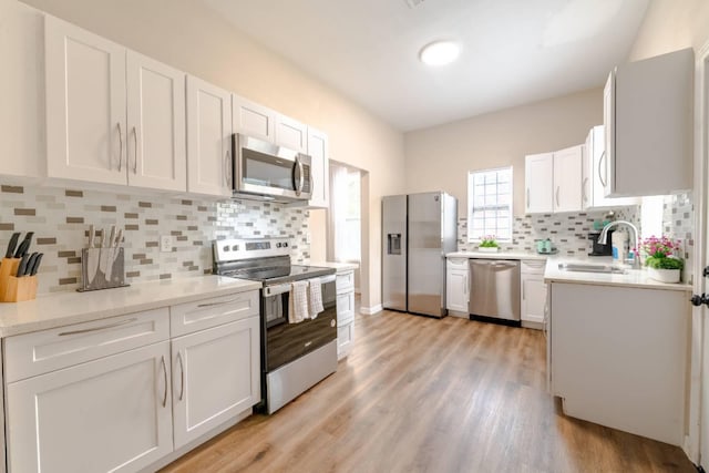 kitchen featuring tasteful backsplash, stainless steel appliances, sink, light hardwood / wood-style flooring, and white cabinetry