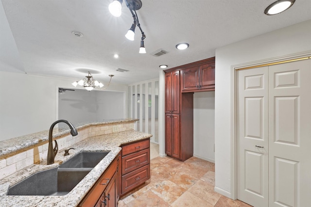 kitchen featuring light stone counters, sink, tasteful backsplash, and an inviting chandelier