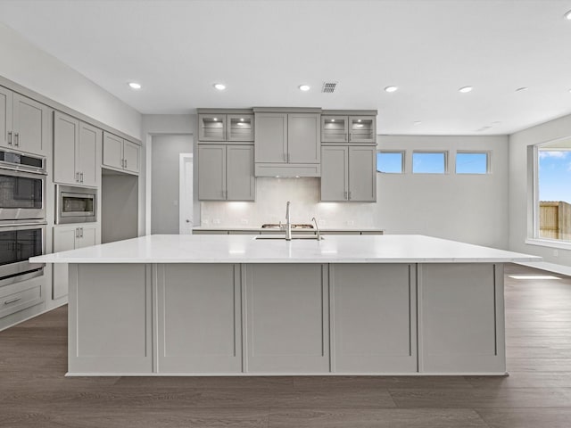 kitchen with gray cabinetry, backsplash, dark hardwood / wood-style floors, appliances with stainless steel finishes, and a large island