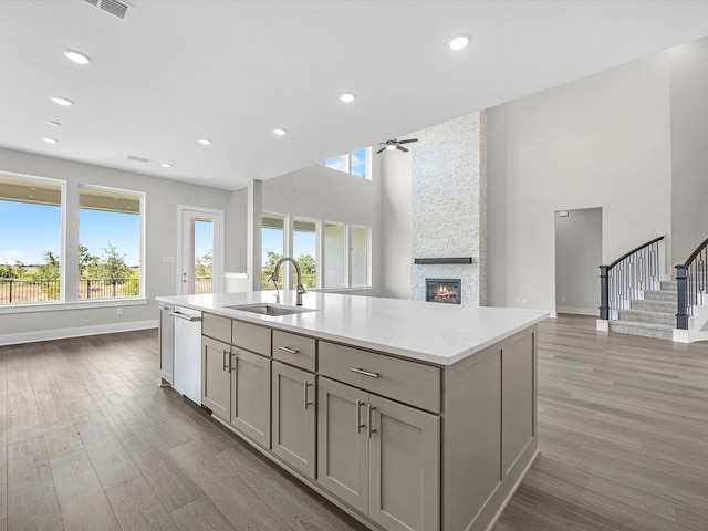 kitchen with ceiling fan, dishwasher, sink, a stone fireplace, and gray cabinets