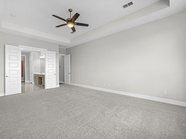 unfurnished bedroom featuring ceiling fan, light colored carpet, ensuite bathroom, and a tray ceiling