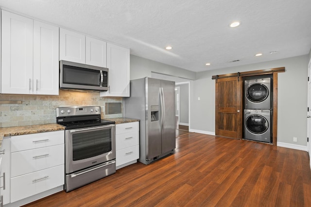 kitchen featuring white cabinets, stacked washer and dryer, decorative backsplash, a barn door, and appliances with stainless steel finishes