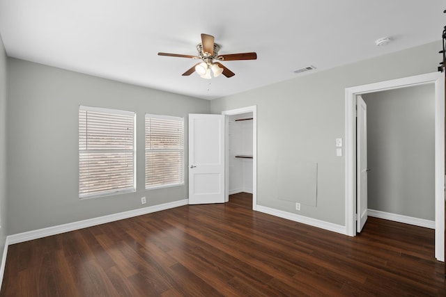 unfurnished bedroom featuring ceiling fan, dark wood-type flooring, a barn door, a spacious closet, and a closet