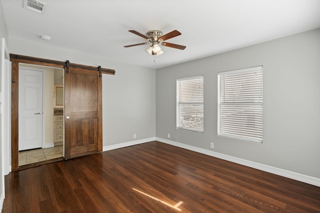 unfurnished bedroom featuring a barn door, ceiling fan, and dark hardwood / wood-style floors