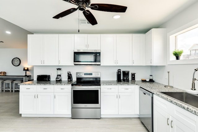 kitchen with appliances with stainless steel finishes, light stone counters, ceiling fan, sink, and white cabinets