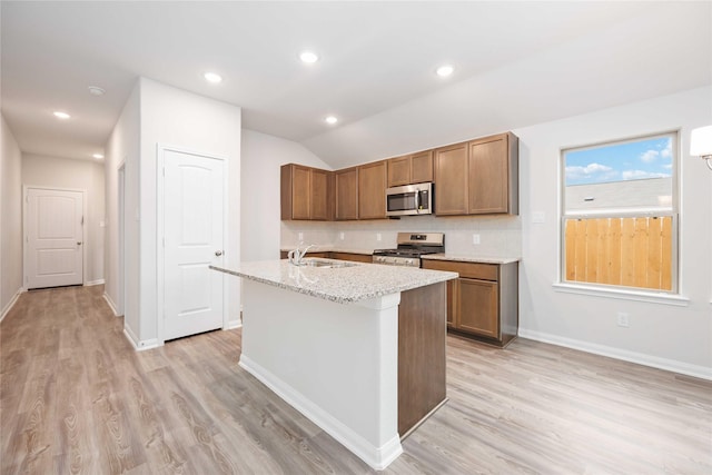 kitchen featuring lofted ceiling, sink, light wood-type flooring, an island with sink, and appliances with stainless steel finishes