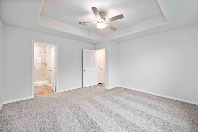 unfurnished bedroom featuring ceiling fan, a raised ceiling, light colored carpet, and connected bathroom