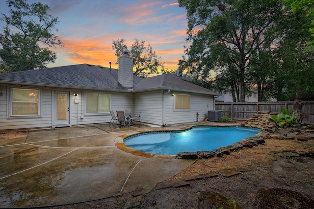 pool at dusk featuring cooling unit and a patio