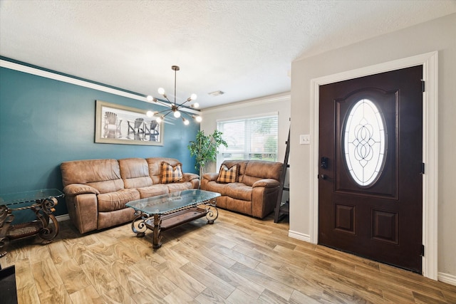 entryway with a textured ceiling, a chandelier, crown molding, and light hardwood / wood-style flooring