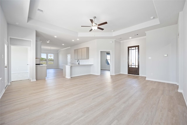 unfurnished living room with a raised ceiling, ceiling fan, and light hardwood / wood-style flooring