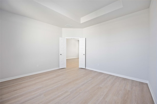 empty room with a tray ceiling and light wood-type flooring