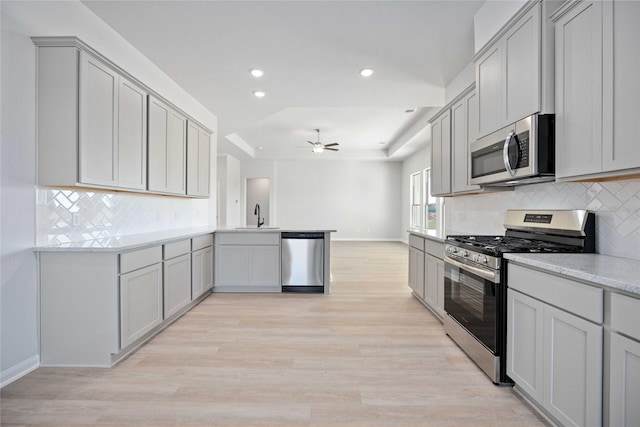 kitchen featuring kitchen peninsula, light wood-type flooring, gray cabinetry, stainless steel appliances, and sink