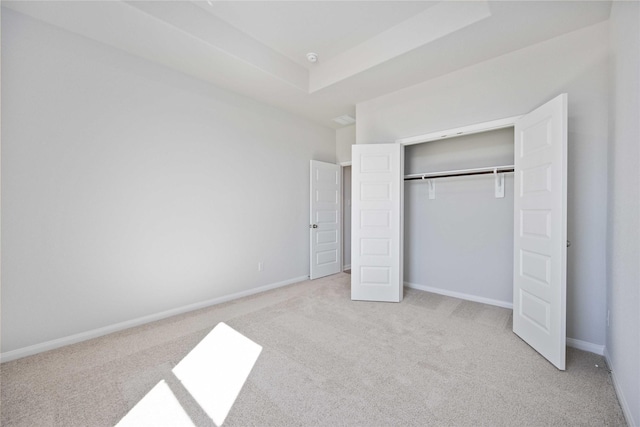 unfurnished bedroom featuring a raised ceiling, light carpet, and a closet