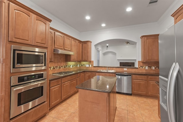 kitchen with appliances with stainless steel finishes, ornamental molding, sink, light tile patterned floors, and a center island