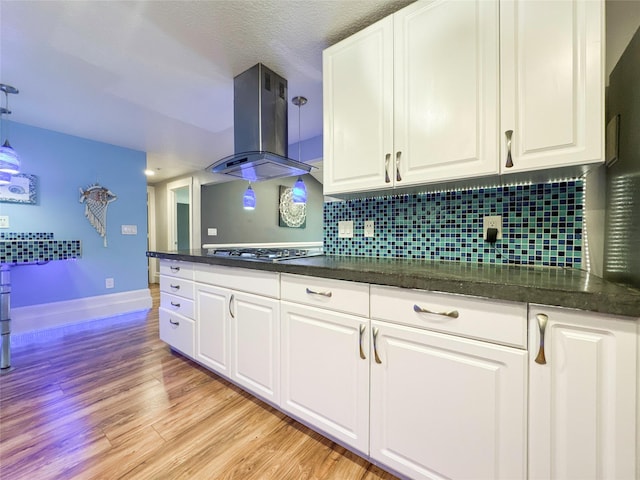 kitchen with decorative backsplash, ventilation hood, stainless steel gas cooktop, white cabinets, and hanging light fixtures