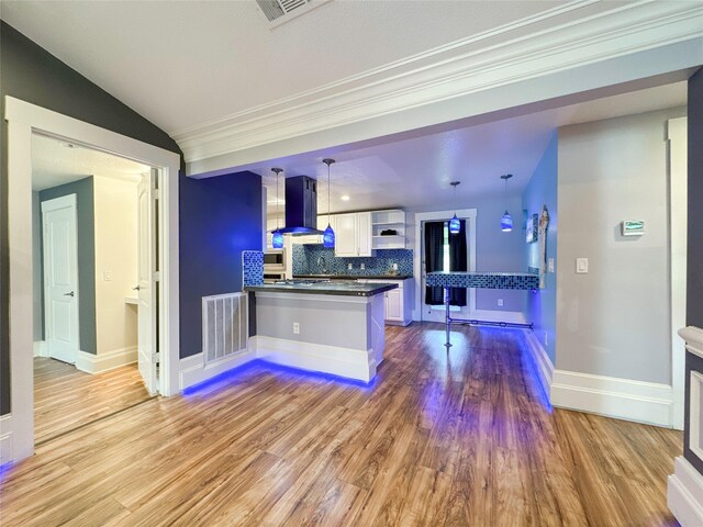 kitchen featuring kitchen peninsula, tasteful backsplash, decorative light fixtures, island range hood, and white cabinetry