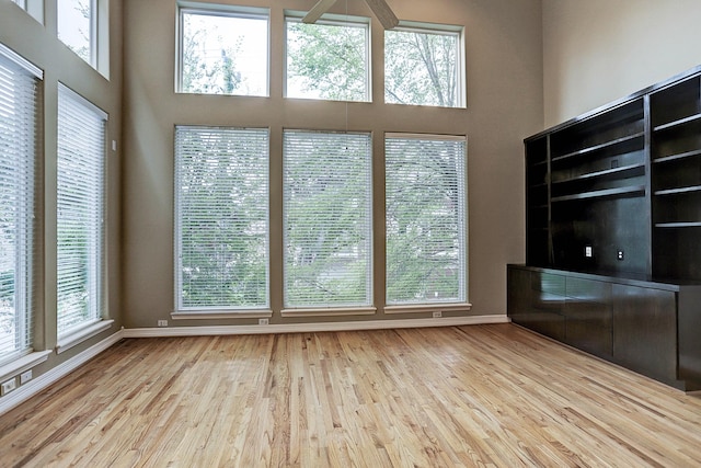 unfurnished living room with ceiling fan, a towering ceiling, and light hardwood / wood-style flooring