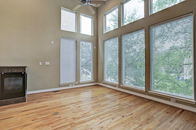 unfurnished living room with ceiling fan, a high ceiling, and light hardwood / wood-style flooring