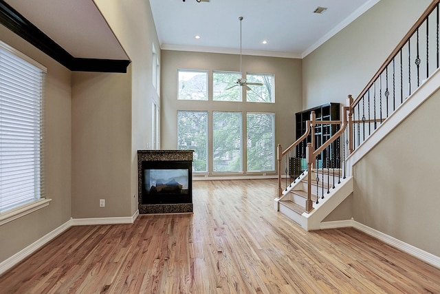 unfurnished living room with a multi sided fireplace, ornamental molding, ceiling fan, and light wood-type flooring