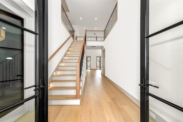 entrance foyer featuring stairs, baseboards, light wood-type flooring, and a towering ceiling