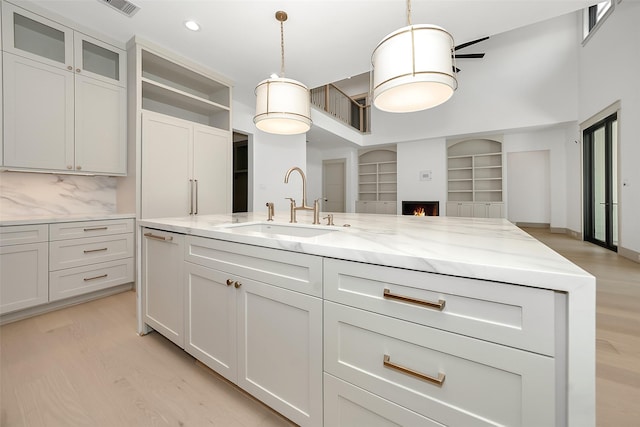 kitchen featuring light stone counters, light wood-style floors, a warm lit fireplace, and a sink