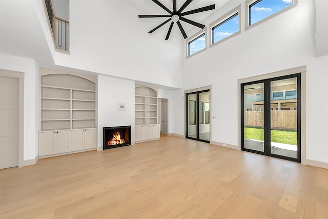 unfurnished living room featuring built in features, light wood-style floors, baseboards, and a lit fireplace