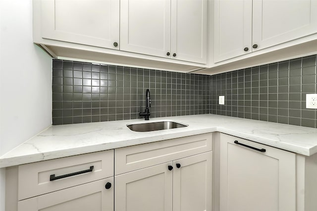 kitchen featuring backsplash, light stone countertops, white cabinetry, and a sink