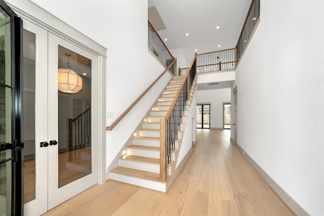 stairway featuring wood finished floors, recessed lighting, french doors, a high ceiling, and baseboards