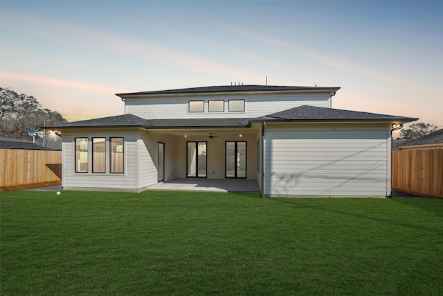 back of house at dusk with a patio, a lawn, and a fenced backyard