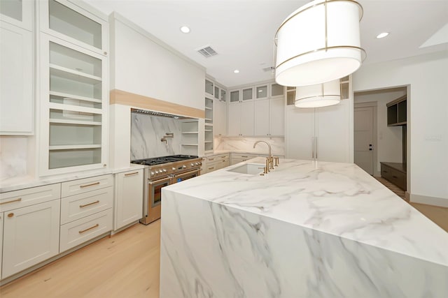 kitchen with visible vents, high end stainless steel range, light wood-style flooring, a sink, and light stone countertops