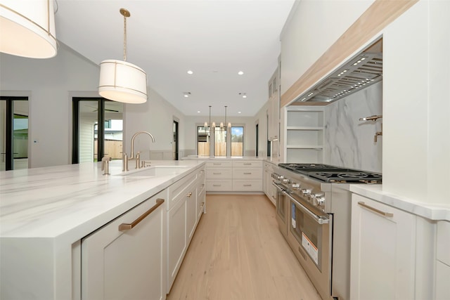 kitchen featuring light wood finished floors, plenty of natural light, a sink, white cabinets, and high end stainless steel range